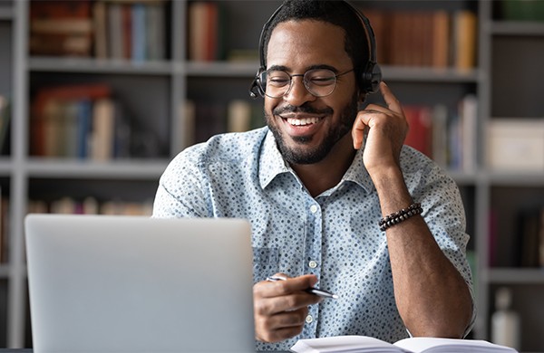 Smiling educator looking at laptop whille wearing headphones.